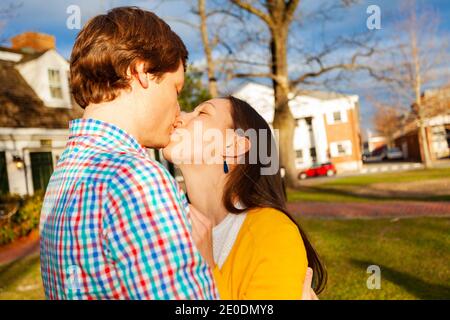 Giovane felice coppia bacio vicino ritratto stand nel parco pubblico vista profilo Foto Stock