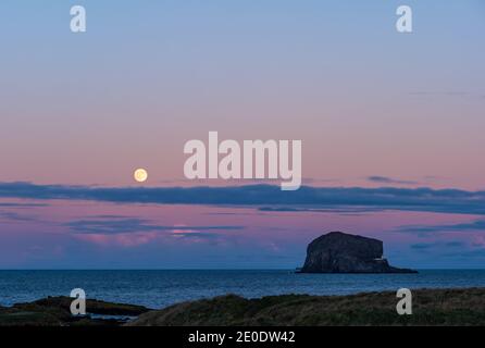 Una luna piena sorge sull'isola di Bass Rock con un colorato tramonto, Firth of Forth, Scozia, Regno Unito Foto Stock