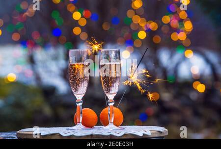 Festeggia la vigilia di Capodanno in giardino all'aperto in inverno, serata innevata, scintillanti sparklers, copy space due bicchieri di flauto con champagne. Foto Stock