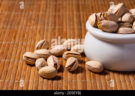 Ciotola bianca di pistacchi salati su stuoia di legno di motivo Foto Stock