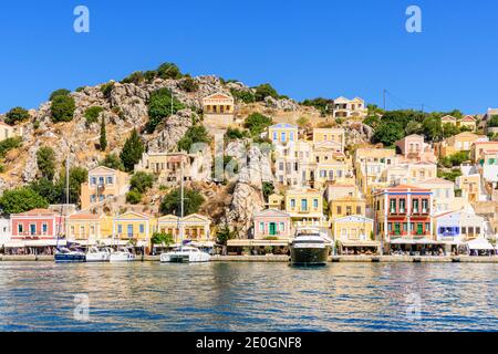 Barche ormeggiate lungo il panoramico lungomare della città di Yialos, sull'isola di Symi, Grecia Foto Stock