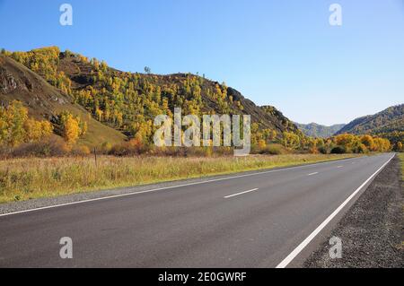 Una strada asfaltata a due corsie attraversa la valle ai piedi delle alte colline. Chuisky, Altai, Siberia, Russia. Foto Stock
