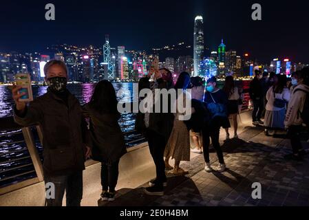 La gente celebra la vigilia di Capodanno indossando maschere protettive sul lungomare del porto di Victoria, nonostante il governo di Hong Kong abbia annullato le celebrazioni dei fuochi d'artificio e limitato le riunioni pubbliche a Hong Kong, in Cina, il 31 dicembre 2020. Hong Kong entra nell'anno 2021 con le più severe regole di distanza sociale COVID-19 e la quarantena estesa per i viaggiatori che arrivano a Hong Kong fino a 21 giorni. Foto Stock