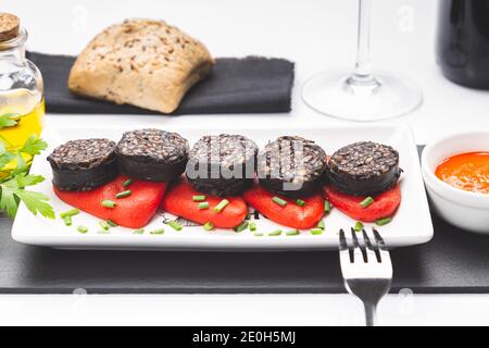 Fette di budino nero spagnolo su peperoni piquillo in piatto bianco su sfondo bianco. Tapas spagnole. Foto Stock