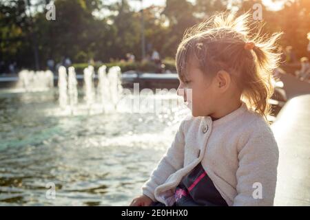 adorabile bambina guarda le fontane nel parco nel parco in una giornata di sole Foto Stock