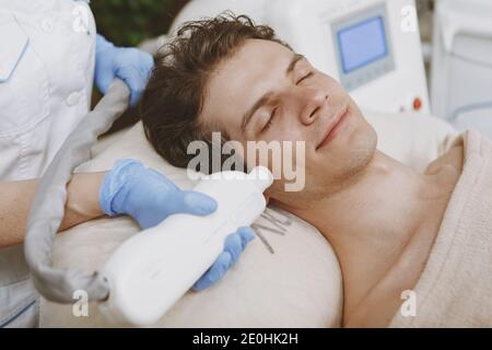 Primo piano di un bell'uomo rilassato che riceve un trattamento laser facciale presso la clinica di cura della pelle. Dermatologo professionista ringiovanente volto del cliente maschile, u Foto Stock