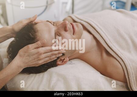 Primo piano di un terapeuta professionale massaggiando templi di un cliente maschile. Bell'uomo che gode di un massaggio testa e viso presso il resort termale. Relax Foto Stock