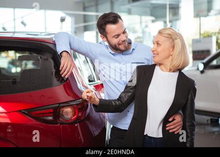 Felice coppia abbracciando, sorridendo l'un l'altro presso la concessionaria. Felice marito e moglie che acquistano una nuova automobile Foto Stock