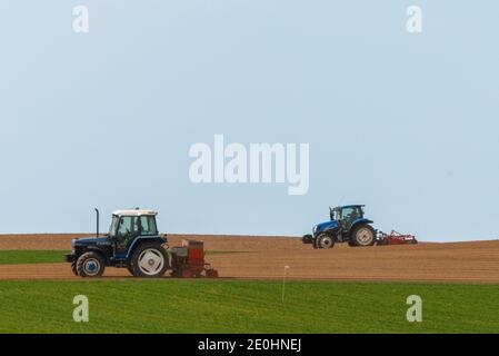 Due trattori blu che arano campi e seminano prodotti nella campagna Foto Stock