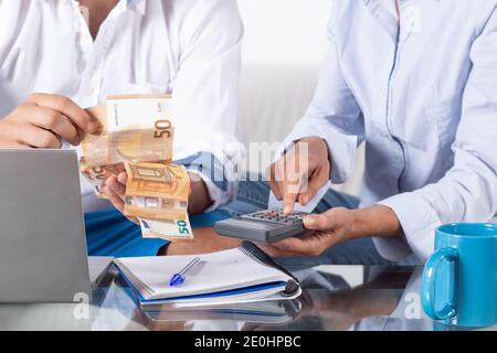 Primo piano donne e uomini´s mani che fanno contabilità con calcolatrice e bollette in mano, sul divano a casa. Foto Stock