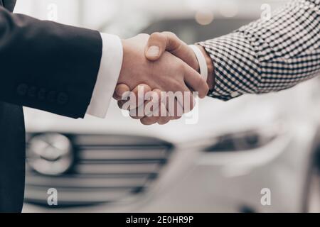 Primo piano di una stretta di mano di due uomini al salone della concessionaria. Il venditore stringe le mani con il cliente dopo aver chiuso la trattativa sull'auto per la vendita. M Foto Stock