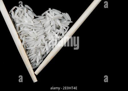 Riso bianco con bastoni cinesi su sfondo nero in la forma di un cuore Foto Stock