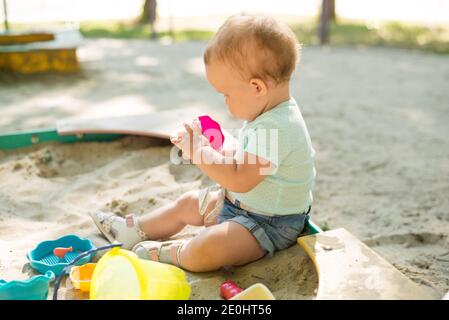 Carina bambina che gioca nella sabbia sul parco giochi all'aperto. Bel bambino che si diverte in una calda giornata estiva soleggiato. Bambino con giocattoli colorati di sabbia. Foto Stock