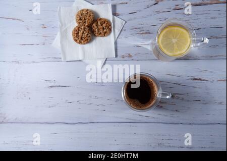 tazza di caffè e acqua con limone e biscotti a grani su sfondo bianco testurizzato Foto Stock