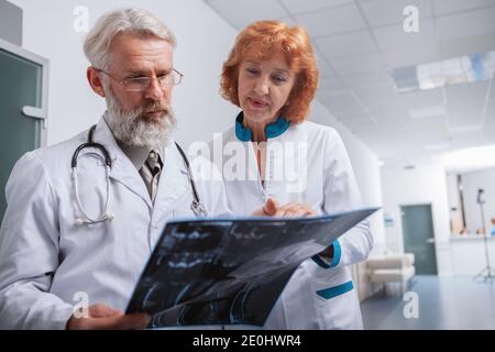 Basso angolo di un medico maschile senior e il suo Collega di sesso femminile che esamina la scansione RM di un paziente insieme a. l'ospedale Foto Stock