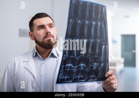 Giovane medico di sesso maschile che esamina la risonanza magnetica di un paziente, lavorando in una clinica moderna Foto Stock