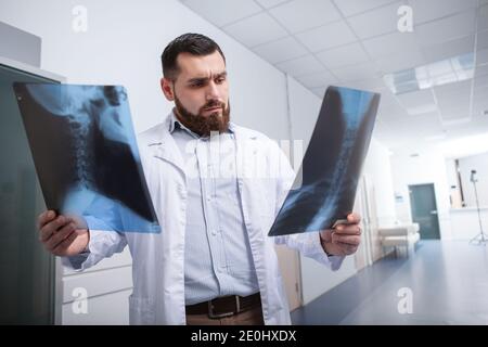 Medico bearded che cammina nel corridoio dell'ospedale, esaminando le scansioni a raggi X. Giovane radiologo maschile che lavora in clinica Foto Stock