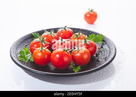 Pomodori ciliegini freschi su piastra rotonda nera, isolati su fondo bianco. Foto Stock