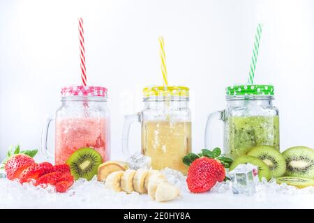 Strawberry Banana fresco e frullati Kiwi, con pezzi di frutta su ghiaccio, isolati su sfondo bianco. Concetto di nutrizione sana. Foto Stock