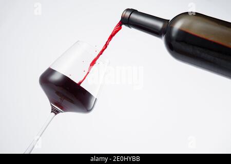Bottiglia di vino rosso versata nel bicchiere, su fondo bianco. Foto Stock
