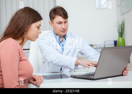 Medico maschile maturo che mostra qualcosa sullo schermo del portatile al suo paziente femminile durante la consultazione medica Foto Stock