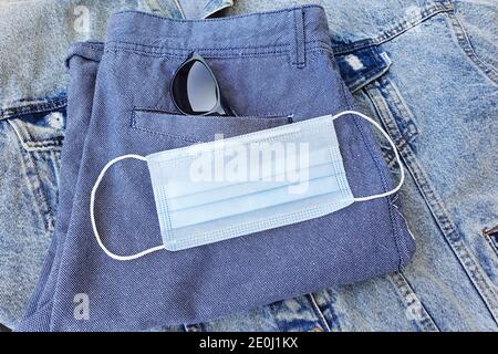 Maschera medica protettiva su pantaloncini blu ripiegati. Accessori nel mondo moderno. Concetto biologico di vita in una nuova realtà. Vista dall'alto, li flatlay Foto Stock