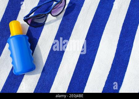 Bottiglia di crema solare e occhiali da sole su un telo da spiaggia a righe. Foto Stock