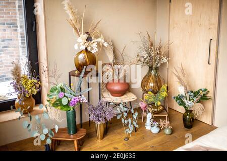 Varietà di diverse composizioni di fiori secchi e freschi e. erbe in una stanza con pareti beige Foto Stock