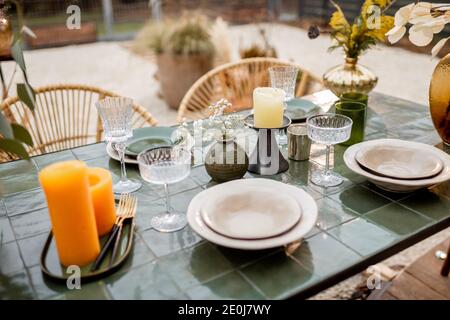 Tavolo decorato in modo festivo in tonalità verdi con candele, erbe e fiori in uno stile naturale Boho all'aperto Foto Stock