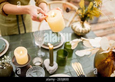 Giovane donna che illumina le candele mentre decorando la tavola da pranzo in naturale Stile boho in toni verdi all'aperto Foto Stock