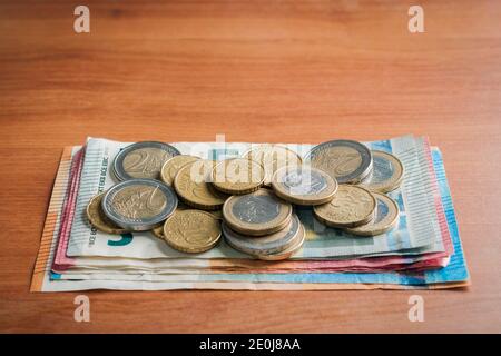 Pila di banconote e monete in euro su un tavolo di legno Foto Stock