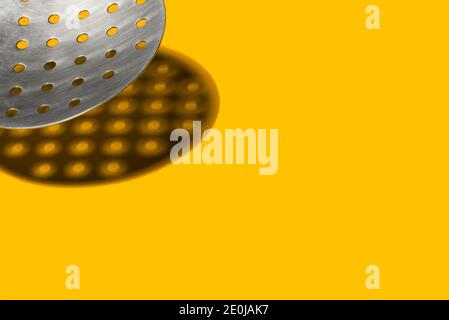 Cucchiaio a taglio con ricci di siviera con ombre dure su sfondo giallo. Utensili da cucina, utensili da cucina. Spazio di copia. Concetto di cibo. Foto Stock