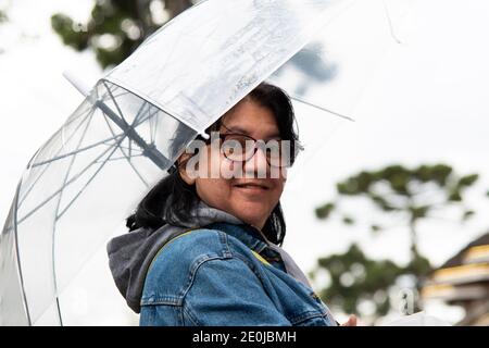 Donna di mezza età che tiene un ombrello trasparente per strada e mostra cielo limpido Foto Stock