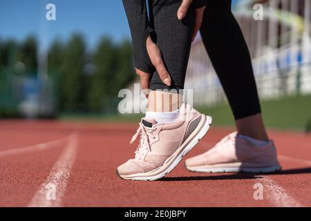 Primo piano di una donna atletica che tocca il piede nel dolore a causa della stesa caviglia. Corsa sport, lesioni da allenamento Foto Stock