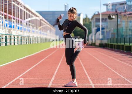 Fit donna stretching muscoli facendo allenamento funzionale, facendo esercizi per le gambe, stretching amstring prima di jogging, in piedi su un tapis roulant gomma st Foto Stock