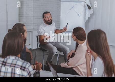 Un uomo d'affari maturo e allegro sorridente, che conduce un incontro d'affari con il suo team creativo in ufficio. Lavoro di squadra, successo, imprenditorialità concep Foto Stock
