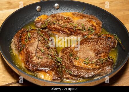 Una padella di tre deliziosi picchetti cotti nel burro in una grande padella su una cucina di legno piano di lavoro Foto Stock