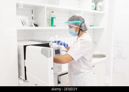 Sterilizzazione di strumenti medicali in autoclave. Operatore medico che indossa una maschera facciale protettiva. Strumenti medici sterili Foto Stock