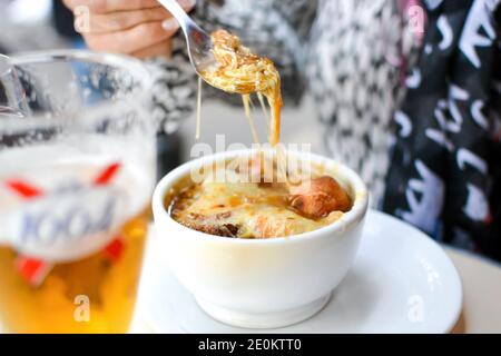 Una donna tiene un cucchiaio su una ciotola deliziosa di Zuppa di cipolle francesi in un caffè all'aperto a Parigi, Francia Foto Stock