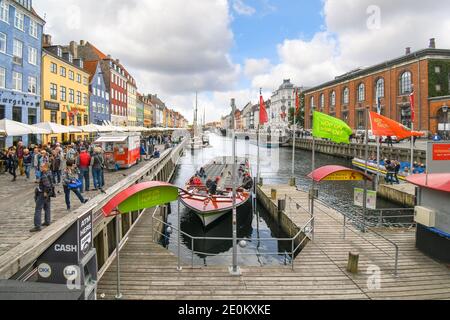 I turisti passeggiata, guida scheda barche e cenare presso caffetterie lungo la strada in una giornata autunnale del xvii secolo waterfront canal Nyhavn a Copenaghen, in Danimarca. Foto Stock