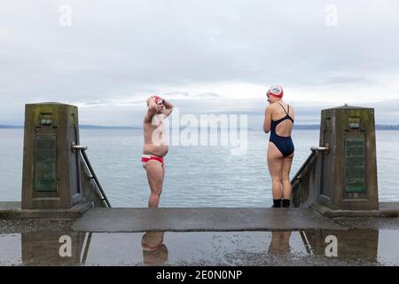 Seattle, Washington, Stati Uniti. 1 gennaio 2021. I bagnanti in mare aperto Sam Day (a sinistra) e Mckinlee parlano di mano prima di immergersi in Puget Sound durante l'annuale nuotata dell'Orso polare di West Seattle presso l'Alki Beach Park. Gli organizzatori hanno organizzato siti fisicamente distanziati e orari sfalsati lungo Alki Beach per i partecipanti in una recente moderazione di casi COVID-19 nella città. Credit: Paul Christian Gordon/Alamy Live News Foto Stock