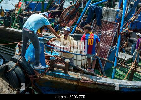 I pescatori scaricano le loro catture da un peschereccio a strascico sul molo del porto trafficato di Essaouira, sulla costa dell'Oceano Atlantico del Marocco. Foto Stock