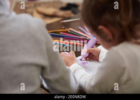 Vista angolare di due bambini che disegnano a casa. Matite colorate sul piano di vetro Foto Stock