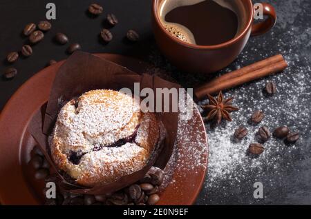 Muffin con mirtilli in piatto marrone e tazza di caldo caffè su sfondo nero Foto Stock