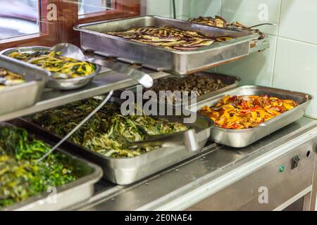 Varietà di verdure cotte, pronte per essere servite da vassoi in acciaio in una cucina industriale Foto Stock