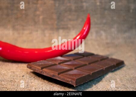 Peperoncino rosso caldo e barretta di cioccolato rotta contro ruvida burlap Foto Stock