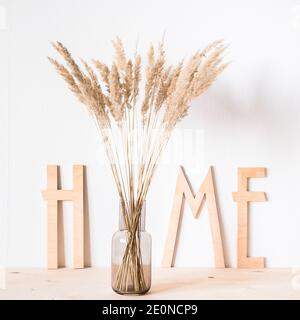 Fiori secchi e lettere di legno a casa sullo sfondo di una parete leggera nello stile del minimalismo Foto Stock