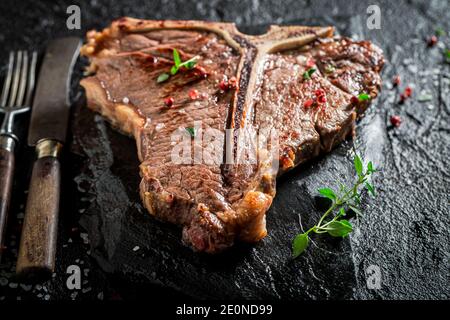 Closeup di bistecca di ossa ben fatta con patatine su nero roccia Foto Stock