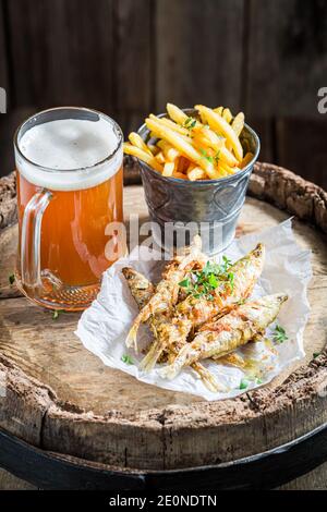 Pesce fritto e patatine fritte con birra leggera su vecchio barile Foto Stock