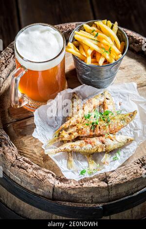 Patatine fritte e pesce fritto puzzato con birra leggera su vecchio barile Foto Stock